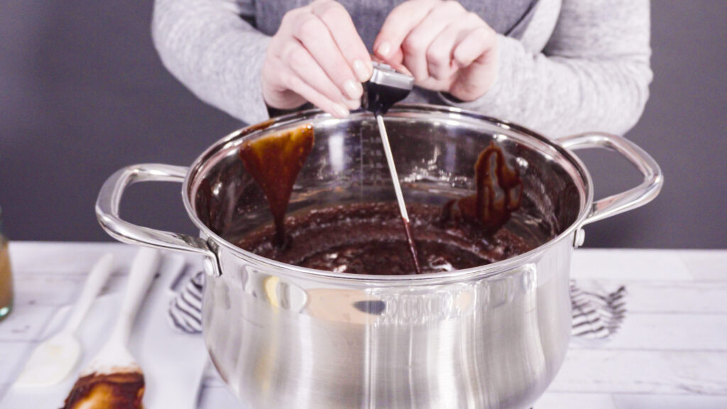 Stirring a mixture of fudge ingredients in a pot over low heat, capturing the crucial cooking process for achieving creamy fudge texture.