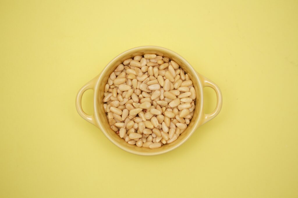 A variety of baking ingredients like almond paste, pine nuts, and egg whites spread out on a wooden background, ready for making pignoli cookies