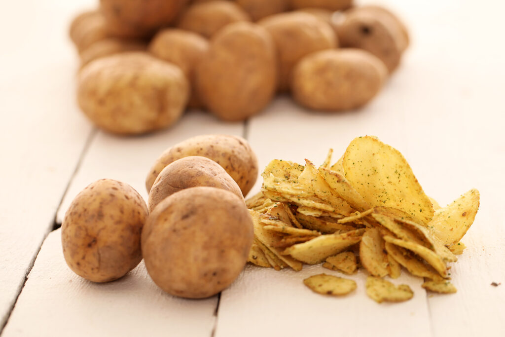 Rustic fresh unpeeled potatoes and chips on a white wooden table