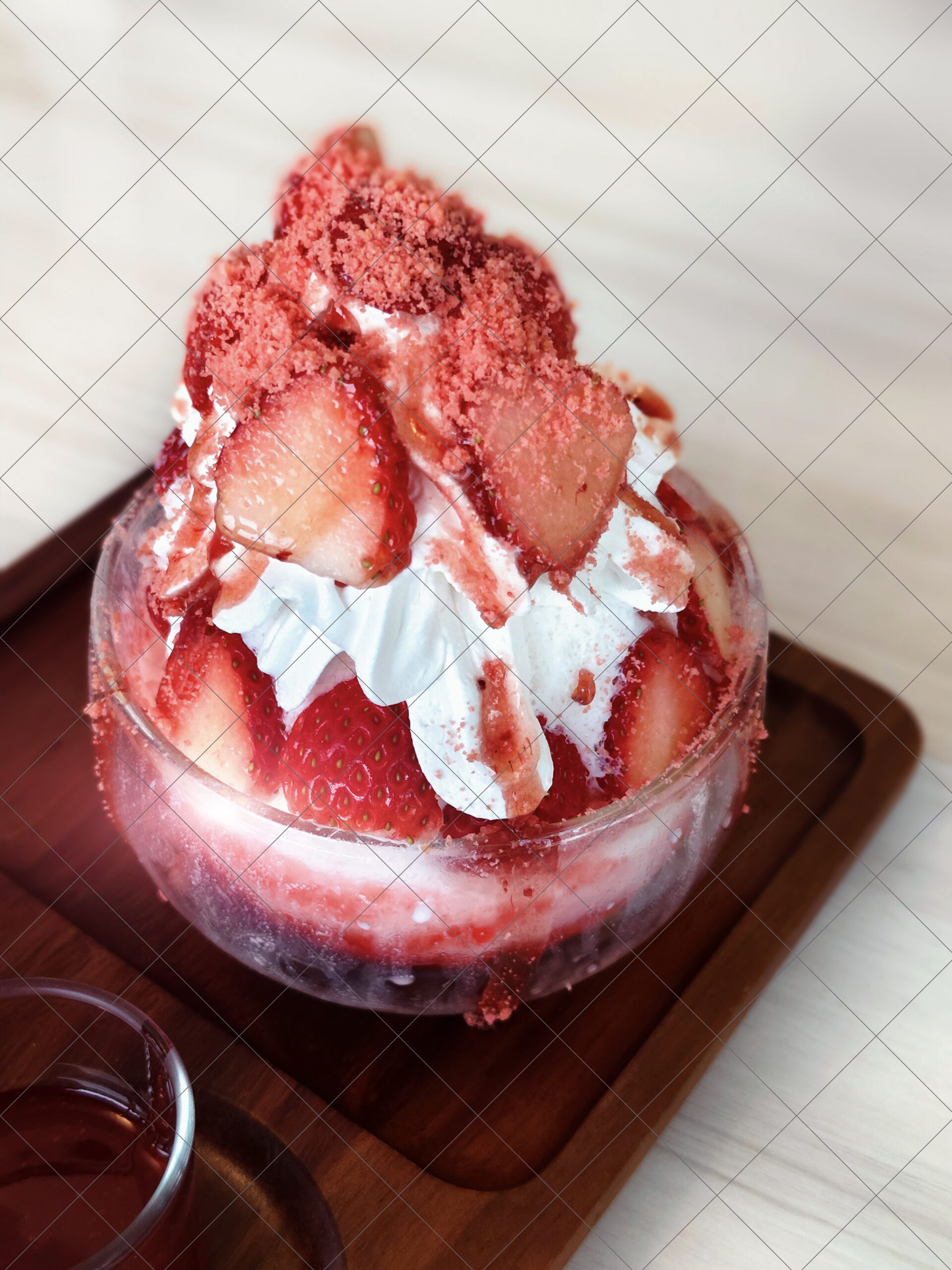 Baskin Robbins Strawberry Shortcake Ice Cream styled as strawberry bingsu in a glass cup on a wooden tray topped with syrup and fresh fruit