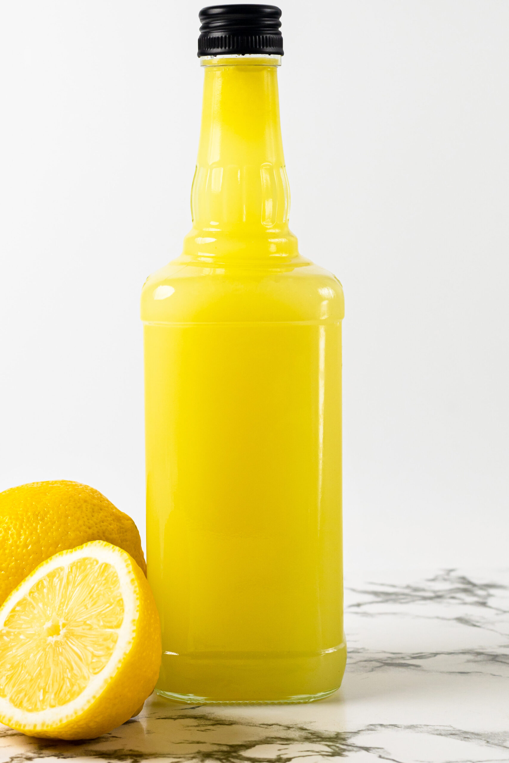 Bottle of fresh limoncello on white plate on marble table